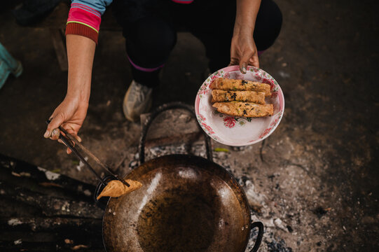 Crop person frying nem rolls in pan on street