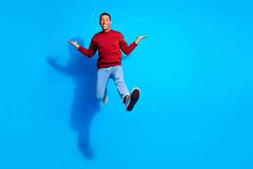 Fototapeta na wymiar Full size portrait of active cheerful young man jump arms hold empty space isolated on blue color background