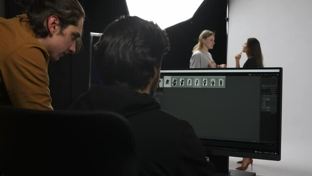 Model and production team in the studio. Retouch and photographer talking checking photos looking at monitor, assistant fixes model makeup.