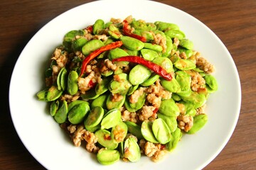 Stir fried stink beans with minced pork dried red chili peppers on top. close up photo top view on wooden background