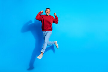 Full length portrairt of carefree sportive person jump raise fists empty space isolated on blue...