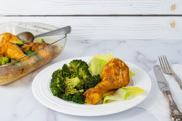 Serving dinner. Close-up view of a plate with an oven-baked chicken drumstick and broccoli served with fresh lettuce