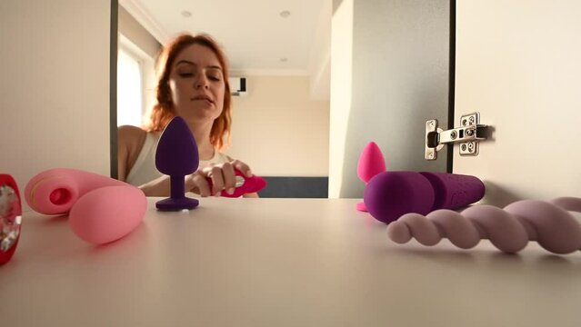 Caucasian red-haired woman opens the closet and chooses a sex toy from her collection. 