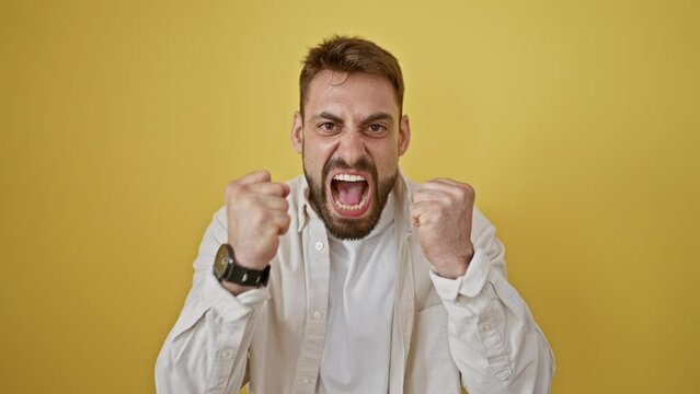Angry young hispanic man, stressed and screaming, standing against a yellow isolated background. portrait of furious expression caught on camera.