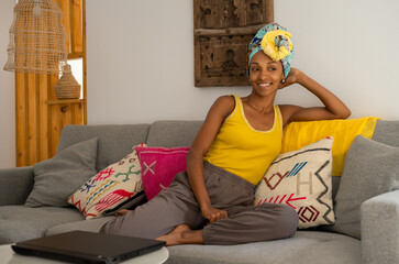 Cheerful casual girl lying on the sofa at home and relaxing. African style young black female model wearing headwrap. - 724960731