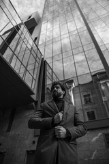 Fototapeta premium Image of a single bearded man in jacket posing behinde higher building. Black and white image.