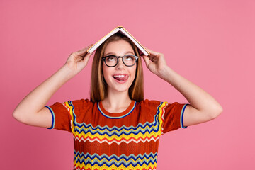 Photo of cheerful overjoyed girl tongue lick teeth hold opened book head isolated on pink color...