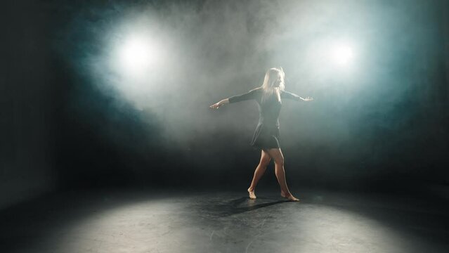Middle aged woman choreographer dancing. Expressive female ballerina dances in black dress in studio on black background. Perform dance element of classical ballet. Choreography diligence concept.