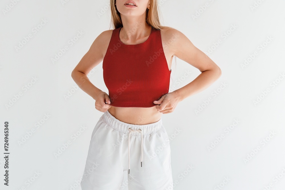 Wall mural A young woman wearing a vibrant top and shorts exudes confidence and style against a minimalist backdrop. Horizontal studio photo.