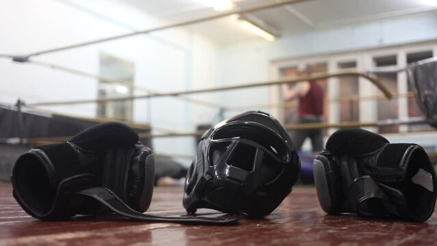Boxing gloves and helmet on the floor, the man in the ring trains (out of focus)
