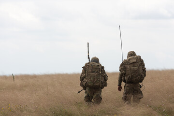 Dos soldados armados de Estados Unidos con uniforme  durante unos ejercicios militares caminan por el campo. - obrazy, fototapety, plakaty