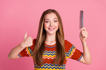 Photo of cheerful cute girl toothy smile hold comb demonstrate thumb up isolated on pink color background