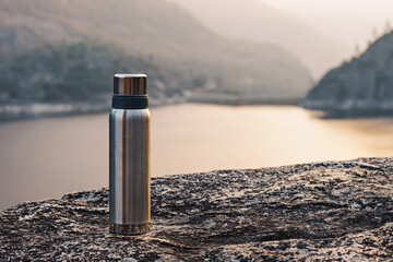 Metal flask for hot drink outdoors, thermos standing with a view
