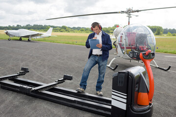 worker with clipboard writing next to helicopter trailer - obrazy, fototapety, plakaty