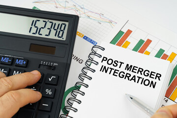 On the table there is a calculator, reports with graphs and a notepad with the inscription - POST MERGER INTEGRATION