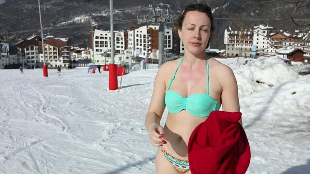 Woman in turquois bikini undress and come on slope near hotels of Rosa Khutor