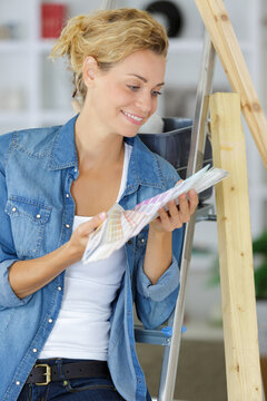 happy woman holding paint swatch booklet at home