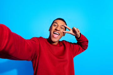 Photo of funky cheerful guy take selfie demonstrate v-sign eye wink blink isolated on blue color background - obrazy, fototapety, plakaty