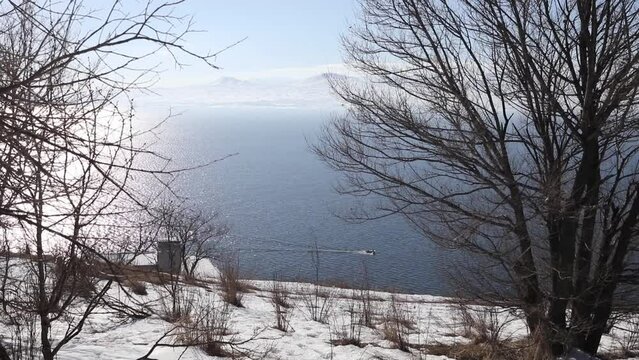 Small boat swim on lake Sevan and mountains afar in Armenia in winter sunny day.