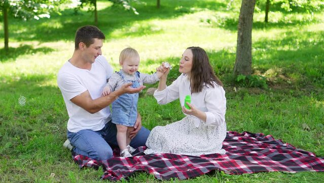 Mom, dad, child play with soap bubbles outdoors in the park. Children playing with soap bubbles, the concept of childhood, relaxation, family vacation.