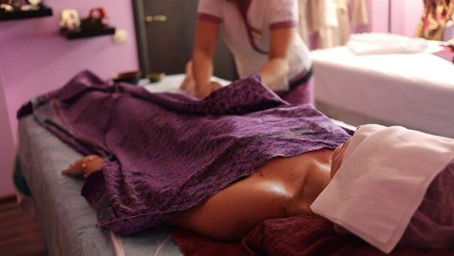 Woman rests in spa, therapist does massage with sand and oils out of focus