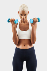 Fototapeta na wymiar Latin American woman lifts dumbbells, young female athlete doing fitness workout, engaged in physical activity to improve health and fitness. Sportswoman do training, isolated over gray background