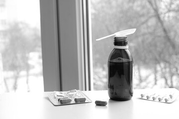 Bottle of cough syrup. Different pills. Blurred winter landscape outside the window. 