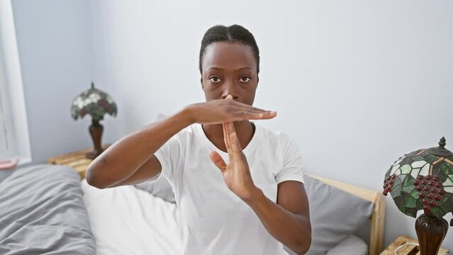 Frustrated african american woman exasperatedly lying in bed showing time-out gesture with hands, comically annoyed in bedroom interior