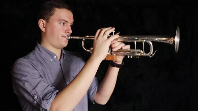 Man in a blue shirt is playing on a trumpet in a dark room