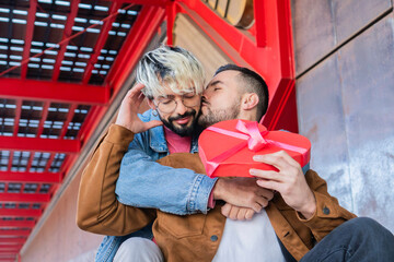 Young adult couple gay sitting outside celebrating valentine's day, his boyfriend is reciving a...