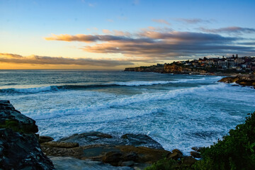 Panoramic dusk view over Tamarama Bay, close to Bondi Beach, Australia with some lone surfers in water and residential area of Bronte in the background