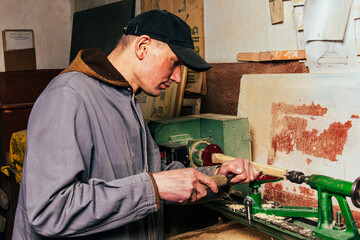 A carpenter works in a workshop with a saw, planer and various tools