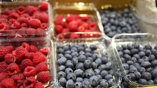 Fresh raspberry and blueberry in plastic containers in food shop, close up
