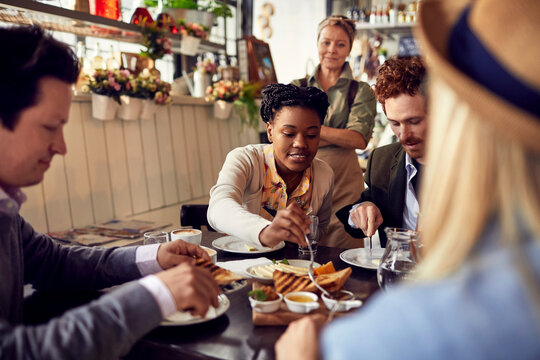 Waitress serving a group of young people eating at a small family restaurant - Powered by Adobe