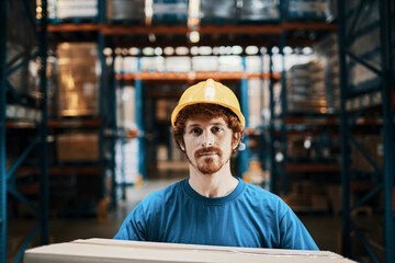Portrait of a young caucasian male warehouse worker holding a cardboard box in a warehouse