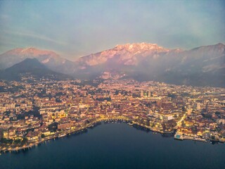 Drone shot of the city of Lecco and snowy mountains in the background.