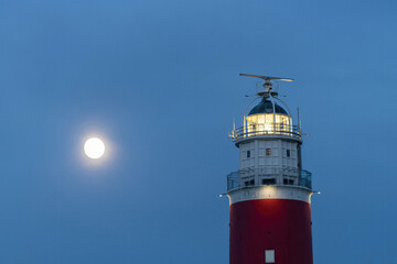 Low angle close up view of light of historical red lighthouse and rising full moon on the island of...