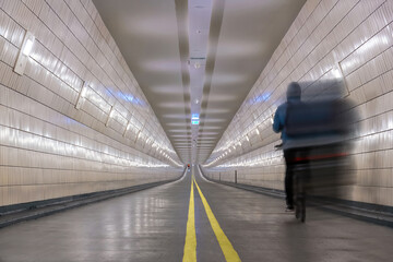 View over the length of a brightly lit modern underground bicycle tunnel with passing distancing...