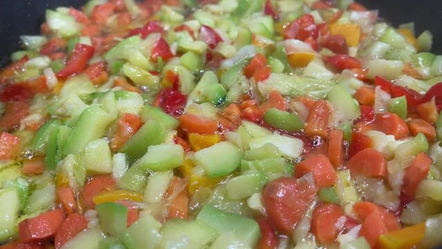 close up of a mixture of chopped vegetables frying in olive oil in a frying pan, zucchini, carrot, leek and peppers, selective focus, horizontal, 4k