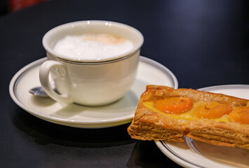 Traditional French pastry or tarte with apricots and a cup of latte, coffee with milk at an artisanal bakery in Strasbourg, Alsace, France