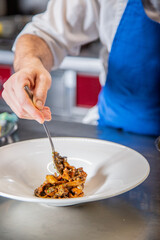Chef prepara setas de temporada salteadas con yema de huevo curada con salsa de soja y flores decorativas sobre un plato de loza blanco