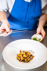 Chef prepara setas de temporada salteadas con yema de huevo curada con salsa de soja y flores decorativas sobre un plato de loza blanco