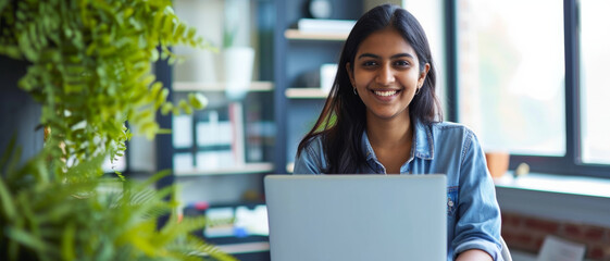 Smiling young indian woman working on a laptop, surrounded by the freshness of indoor plants - Powered by Adobe