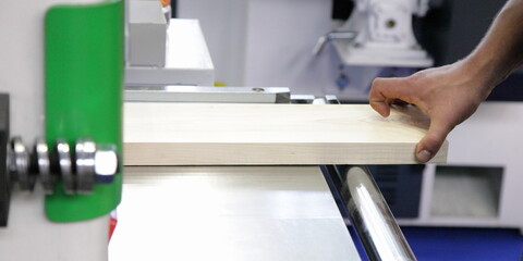The carpenter's hand feeds the workpiece into a hand-held woodworking machine for planing a board