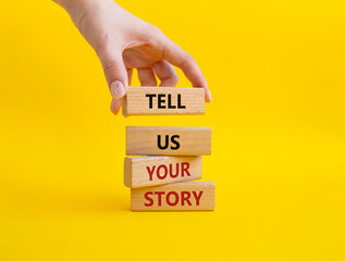 Tell us your story symbol. Concept words Tell us your story on wooden blocks. Beautiful yellow background. Businessman hand. Business and Tell us your story concept. Copy space.