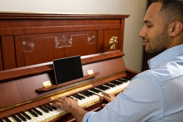Man sitting at piano and playing at home using tablet