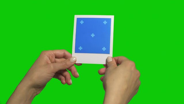 Holding Instant Photo Frame in Hands Evaluating and Considering from different angles. Isolated on green screen with blues screen backdrop with trackers on photo frames.
