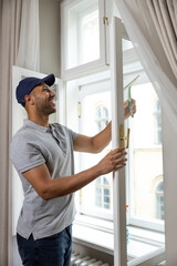 Young man in cap and T-shirt washing window at home with wiper squeegee.