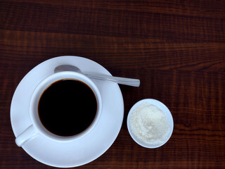 Top view of cup of black coffee, spoon on the Pyrex and bowl with sugar on the wooden table with copy space for design.
