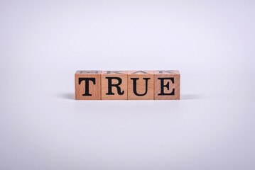 The inscription True made of wooden cubes on a plain background
